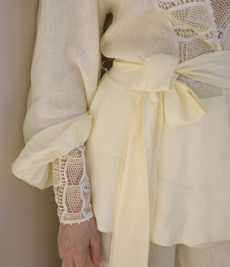 Detalhe do laço na cintura e do punho em renda de uma blusa da marca.