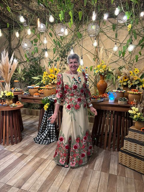 Cliente em vestido longo bordado com flores em tons de vermelho e verde.