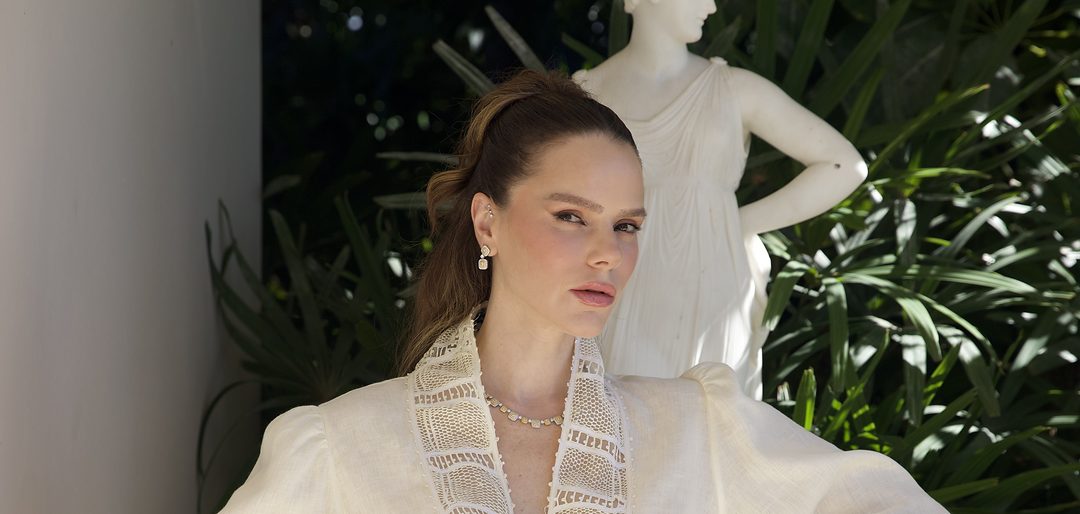 Modelo em jardim, com blusa de linho e gola em renda renascença, ao lado de uma escultura de mármore.